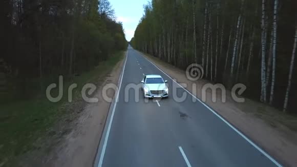 从无人驾驶白车上观看车前灯在穿过绿色森林的道路上行驶视频的预览图