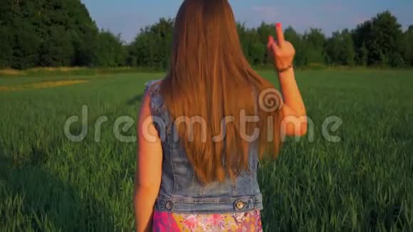 一个长着一头直发的年轻女孩在日落时分站在田野里视频的预览图
