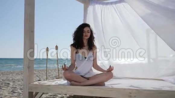 瑜伽女在平房里在热带岛屿上在海和沙的背景下夏天风会长出头发和白布视频的预览图