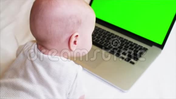 6个月大的男婴躺在笔记本电脑前的床上上面有彩色键盘屏幕视频的预览图