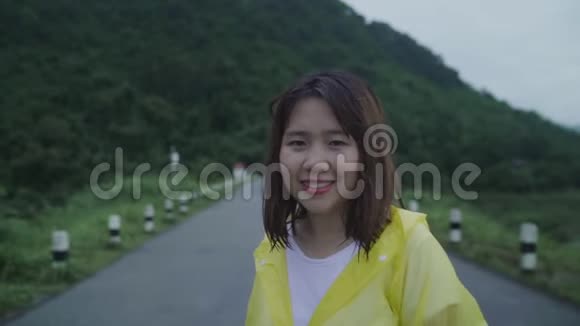 慢动作年轻的亚洲妇女感到高兴的打雨而穿着雨衣走在森林附近视频的预览图
