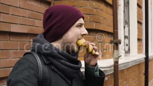 一个男人喝咖啡吃牛角面包站在巷子里的房子附近视频的预览图