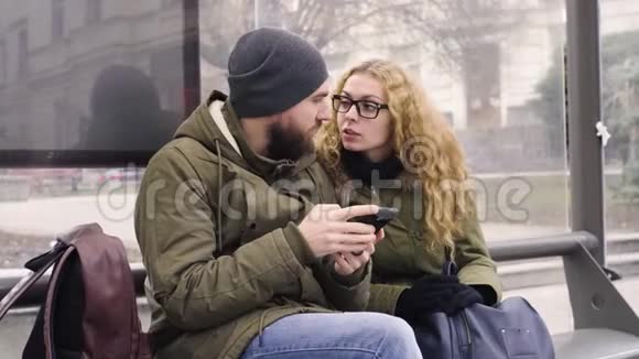 男青年和女青年在公共汽车站等候时使用手机视频的预览图
