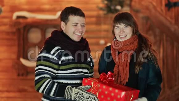 男孩和女孩给观众一个红色的圣诞礼物背景是一个童话般的房子圣诞节和新视频的预览图