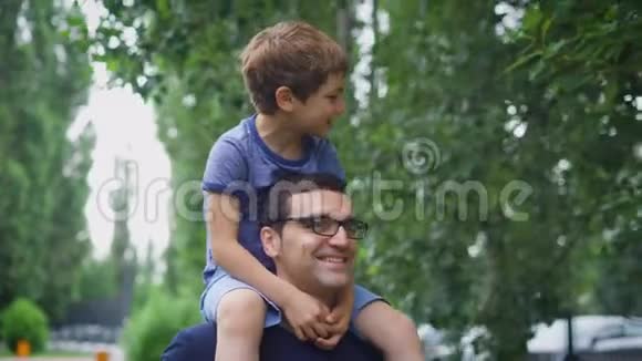 一个快乐而成年的男人把他的小儿子扛在肩上一个男孩喜欢在男人身上度过他暑假视频的预览图