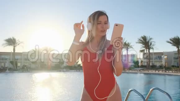 穿红色泳衣和耳机的美女肖像使用应用程序在智能手机上跳舞和听音乐比基尼视频的预览图