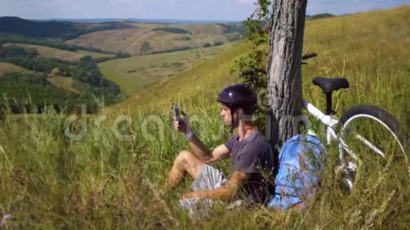 一个年轻人骑自行车旅行时正在树下休息他手里拿着一部手机视频的预览图