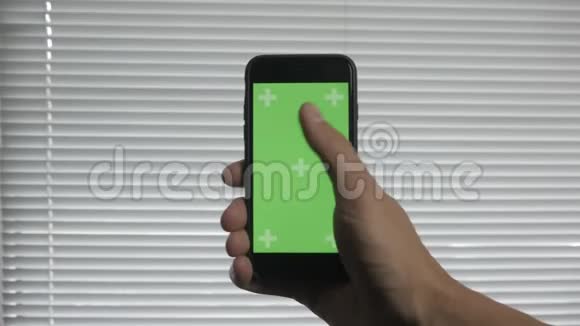 在百叶窗的背景下特写男性手触摸智能手机绿色屏幕Chroma键视频的预览图
