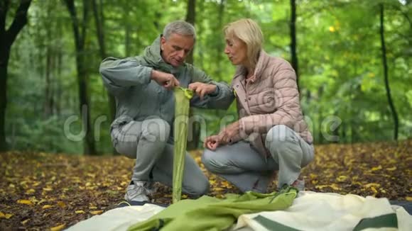 一对漂亮的资深运动家夫妇在森林里搭帐篷视频的预览图