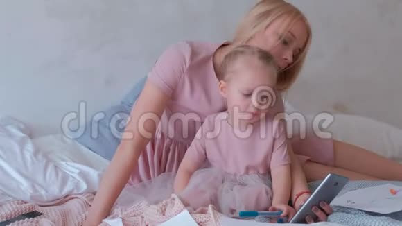 年轻迷人的金发妈妈在手机上给她穿着粉红色裙子的迷人小女儿展示一些东西视频的预览图