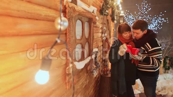 一对相爱的夫妇坐在一个木制仙女的房子的背景上用热饮料加热杯子圣诞节和新年视频的预览图