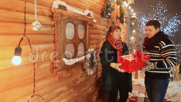一对相爱的夫妇坐在木仙房的背景上扔一份红色的礼物圣诞节和新年主题视频的预览图