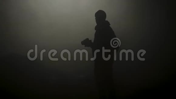 黑色轮廓的人站在烟雾弥漫的黑暗中库存录像年轻男子神秘的轮廓在黑暗中闪耀视频的预览图