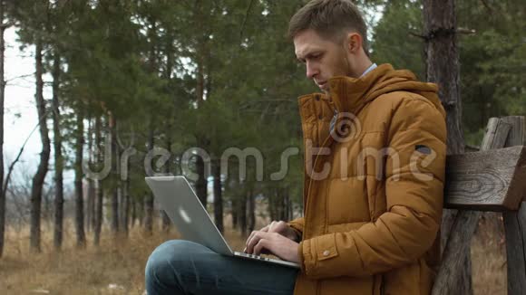 穿领带的男士商人在秋天的树木背景下在公园的长椅上使用笔记本电脑视频的预览图
