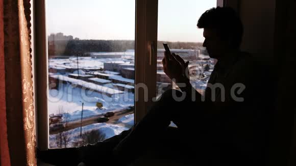 一个拿着手机坐在窗台上的男人的剪影视频的预览图