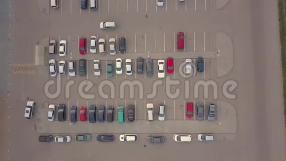 在购物中心附近的停车场上空俯瞰大量不同品牌和颜色的汽车视频的预览图