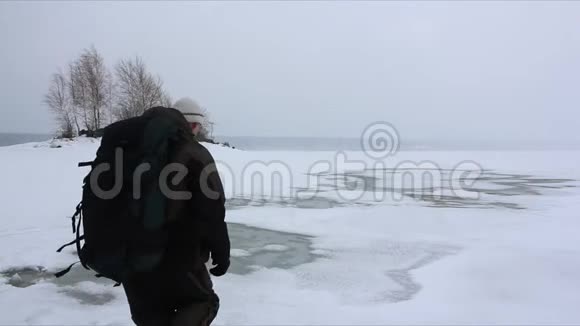 背着背包的人在融化的河面上的暴风雪中行走视频的预览图