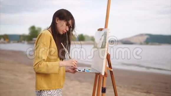 年轻的女画家在河岸上画风景视频的预览图