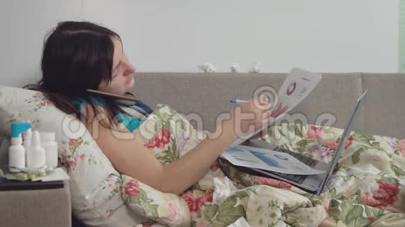 生病的女人躺在家里的床上用电话和笔记本电脑工作视频的预览图