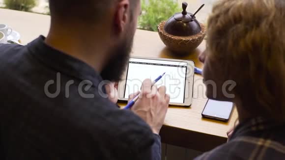 一对男女坐在咖啡馆里在平板电脑上研究图表的特写镜头视频的预览图