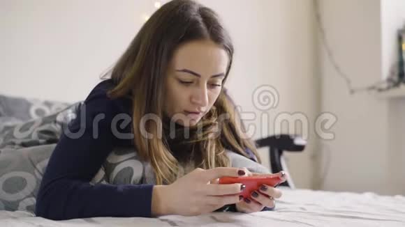 躺在毯子下躺在床上用手机打字的年轻姑娘视频的预览图