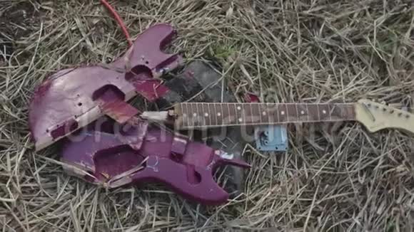 关闭破碎的紫色吉他躺在枯萎的干草上俯视库存破电吉他部件紫罗兰甲板视频的预览图