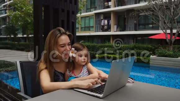 快乐的母亲和女儿在游泳池附近休息慢动作使用笔记本电脑视频的预览图