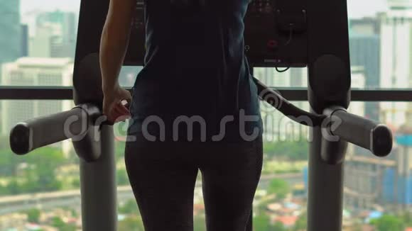 一位年轻女子在一座摩天大楼顶部的健身房里在跑步跑道上训练观看整个城市的景色视频的预览图