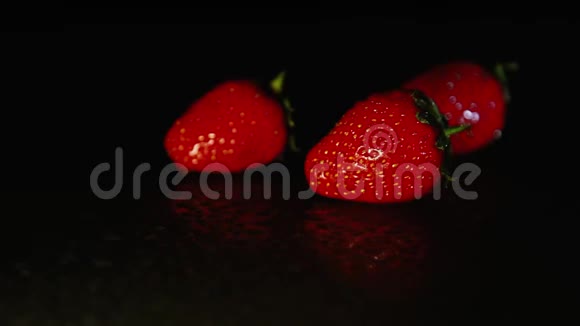三个草莓浆果在黑暗中躺在潮湿的表面上黑色背景视频的预览图