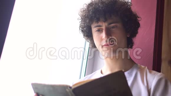 穿着白布的年轻绅士坐在窗台上用窗外的日光阅读书籍视频的预览图