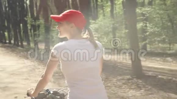 快乐活泼活泼的年轻女子在夏日阳光明媚的公园里骑着红帽子自行车视频的预览图
