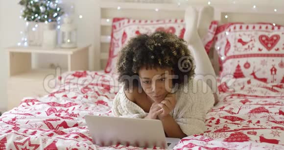 漂亮的女人在床上看手提电脑视频的预览图