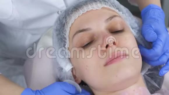 美容师用棉垫擦拭一个年轻女人的脸美容师戴手套和面部特写视频的预览图