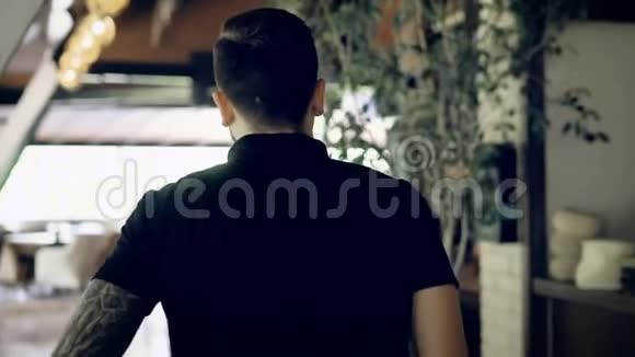 年轻男子穿着黑色t恤双手撑着腰穿过咖啡馆走到他的两名妇女视频的预览图