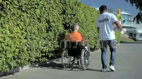 一个愉快的志愿者帮助一个坐在轮椅上的人的后视镜视频的预览图