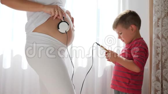 孕妇通过耳机手机小男孩手中的小男孩把音乐送给肚子里的宝宝视频的预览图