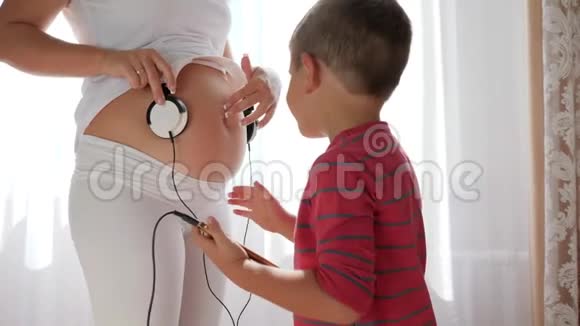 白衣女子通过耳机手机小男孩的手把音乐送给肚子里的宝宝视频的预览图