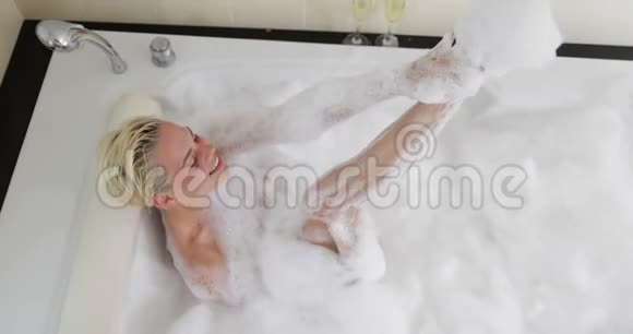 沐浴的年轻女性在沐浴中放松充满泡沫的抬起腿的视角微笑的美丽女孩在家享受水疗视频的预览图