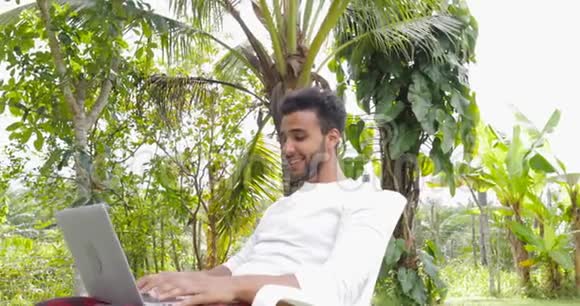 在热带花园中使用笔记本电脑户外工作的年轻人视频的预览图