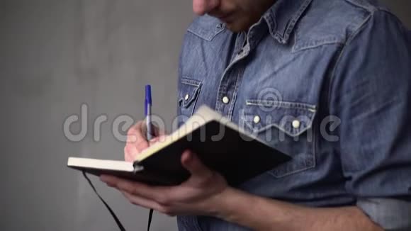 那家伙的PAN在笔记本上写字而站在灰色墙壁对面的窗户附近视频的预览图