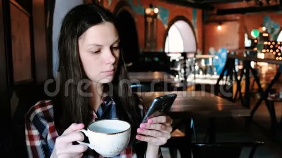 布鲁内特女士穿着格子衬衫从一个大杯子里喝茶看着电话视频的预览图