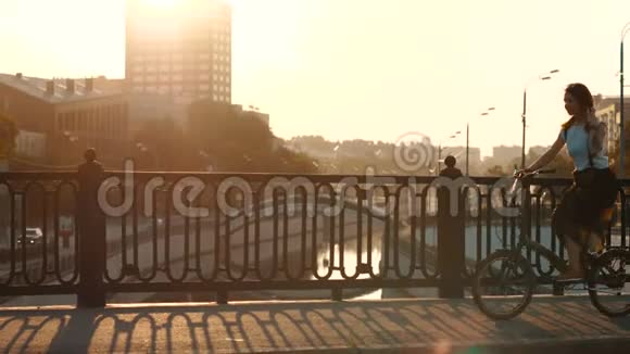 背景建筑与阳光下的城市桥上骑自行车的年轻女子视频的预览图
