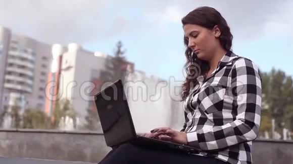 年轻快乐的女孩在城市里有笔记本电脑坐在喷泉旁边喝咖啡视频的预览图