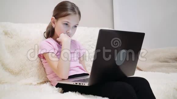 小女孩坐在沙发上看笔记本电脑上的插图视频的预览图
