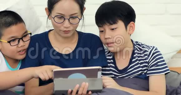 快乐的亚洲家庭姐妹和兄弟与朋友玩平板电脑在家微笑着面对视频的预览图