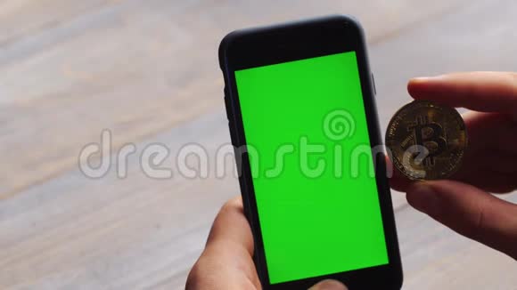 人使用垂直智能手机与绿色屏幕男子手拿手机和一枚金币的特写镜头视频的预览图