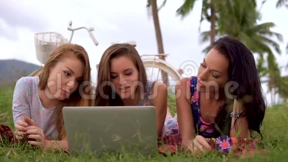 在农村野餐时妇女们一起用笔记本电脑躺在草地上视频的预览图