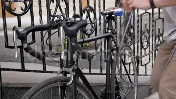 4k视频年轻的嬉皮士把他那辆老式的黑色自行车锁在街道上的栅栏上视频的预览图
