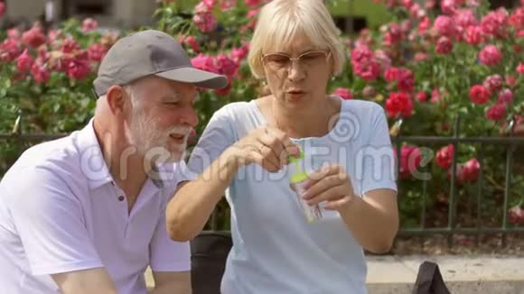 快乐的家庭享受假期老两口坐在公园的长凳上吹着肥皂泡视频的预览图