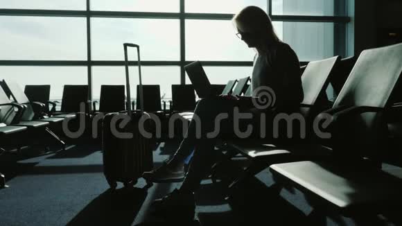 女商人在机场候机楼用笔记本电脑工作在等我的航班剪影背景下的一个视频的预览图